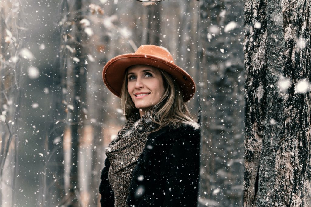 Mujer con gorro naranza en un bosque mientras nieva